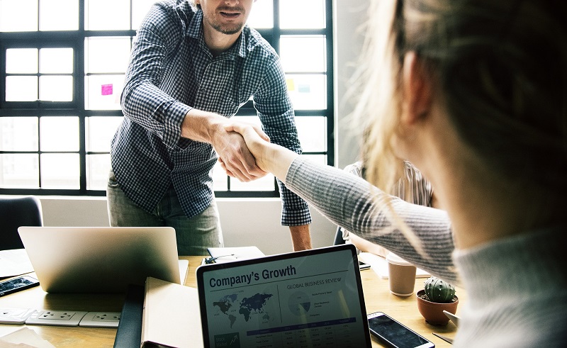 Two people shaking hands across a table with laptops open