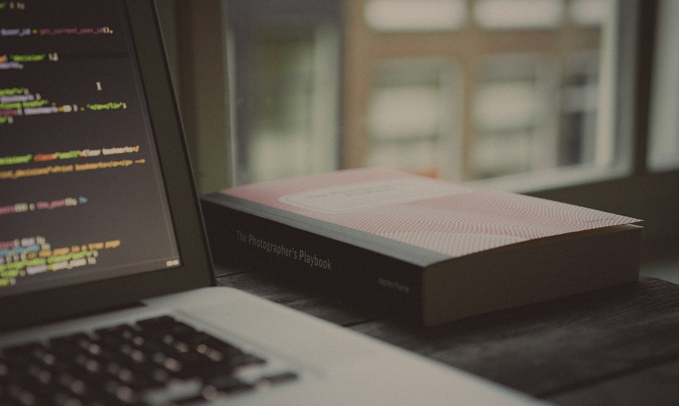 An open laptop showing computer code next to a large book